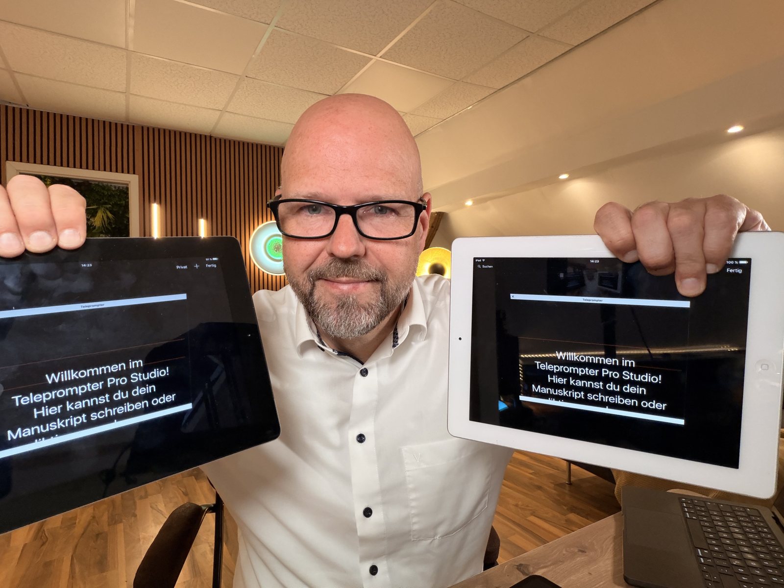 Bodo Kern standing in his studio, holding up two older tablets that show the teleprompter text